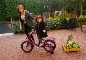 Dzieci przewożą warzywa rowerem na wózku.