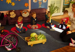 Dzieci przewożą warzywa rowerem na wózku.